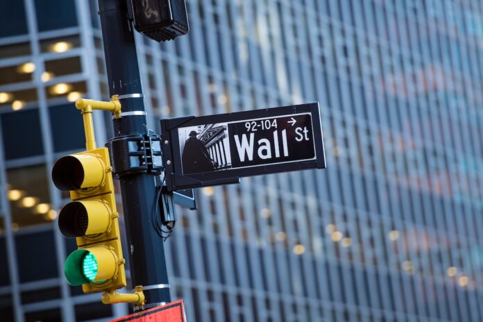 Wall street sign in the foreground and a huge blurred building in the background in Manhattan, New York, USA.